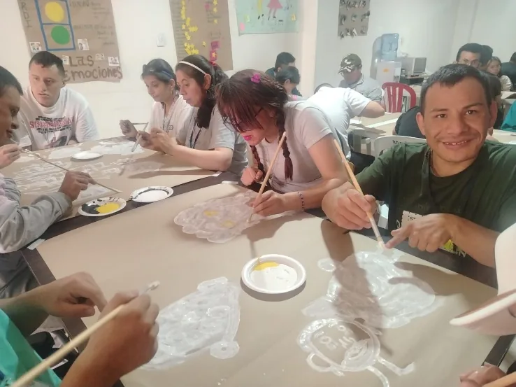 Jóvenes pintando con pincel sobre una mesa en el taller de artes plásticas