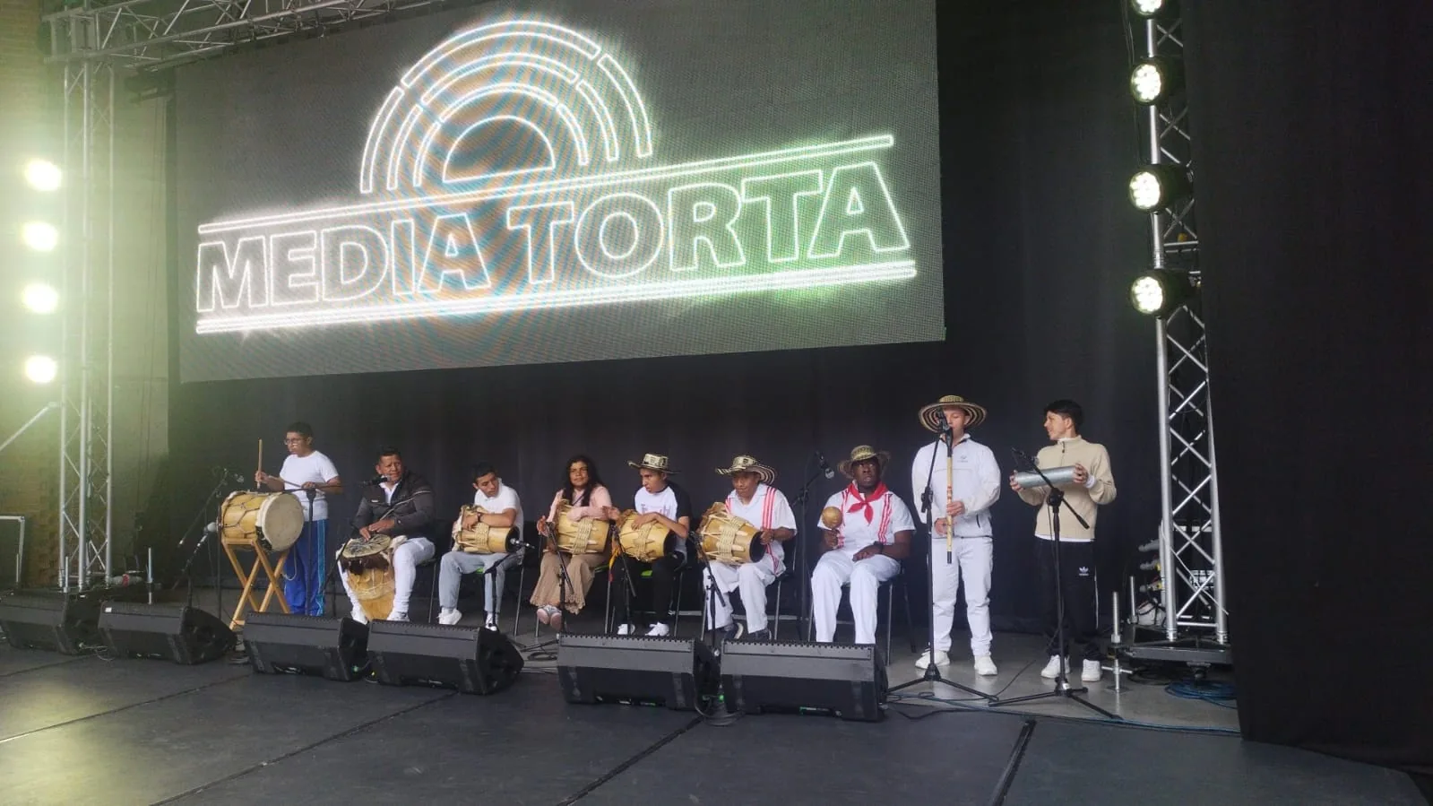 Grupo tocando tambores y gaitas en el escenario de la Media Torta, con luces y pantalla gigante